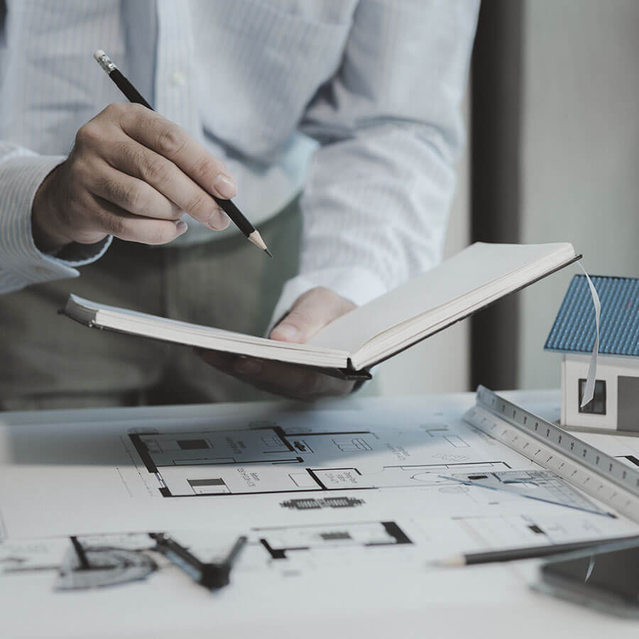 Architecte prenant des notes dans un carnet au dessus des plans de la maison